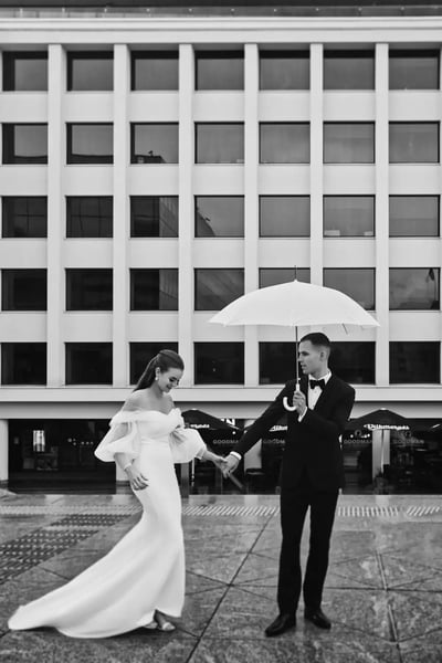 Vestuvių fotografas Kaune: nuotaka ir jaunikis su skėčiu lietuje Vienybės aikštėje, nespalvota nuotrauka
