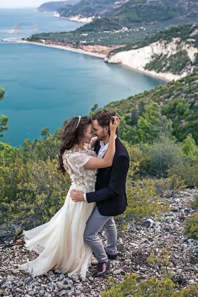 Vestuvių fotografas užsienyje: apsikabinę jaunavedžiai ant kranto uolų virš jūros įlankos Italijoje