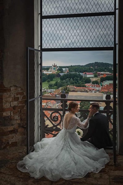 Vestuvių fotografas Vilniuje: jaunavedžiai sėdi prie lango varpinėje, už jų atsiveria miesto stogų vaizdas