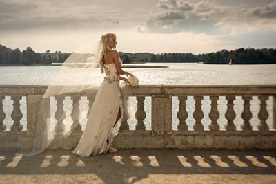Vestuvių fotosesija prie ežero: nuotaka su šydu ant balustrados saulėlydžio šviesoje